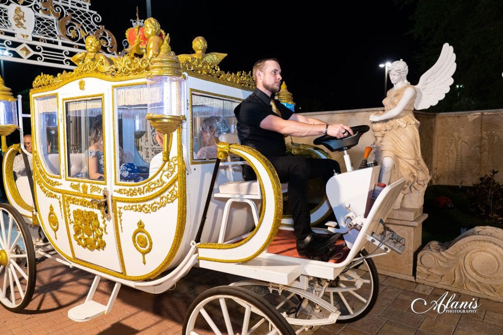 White and gold royal carriage lit up at night beside an angel statue